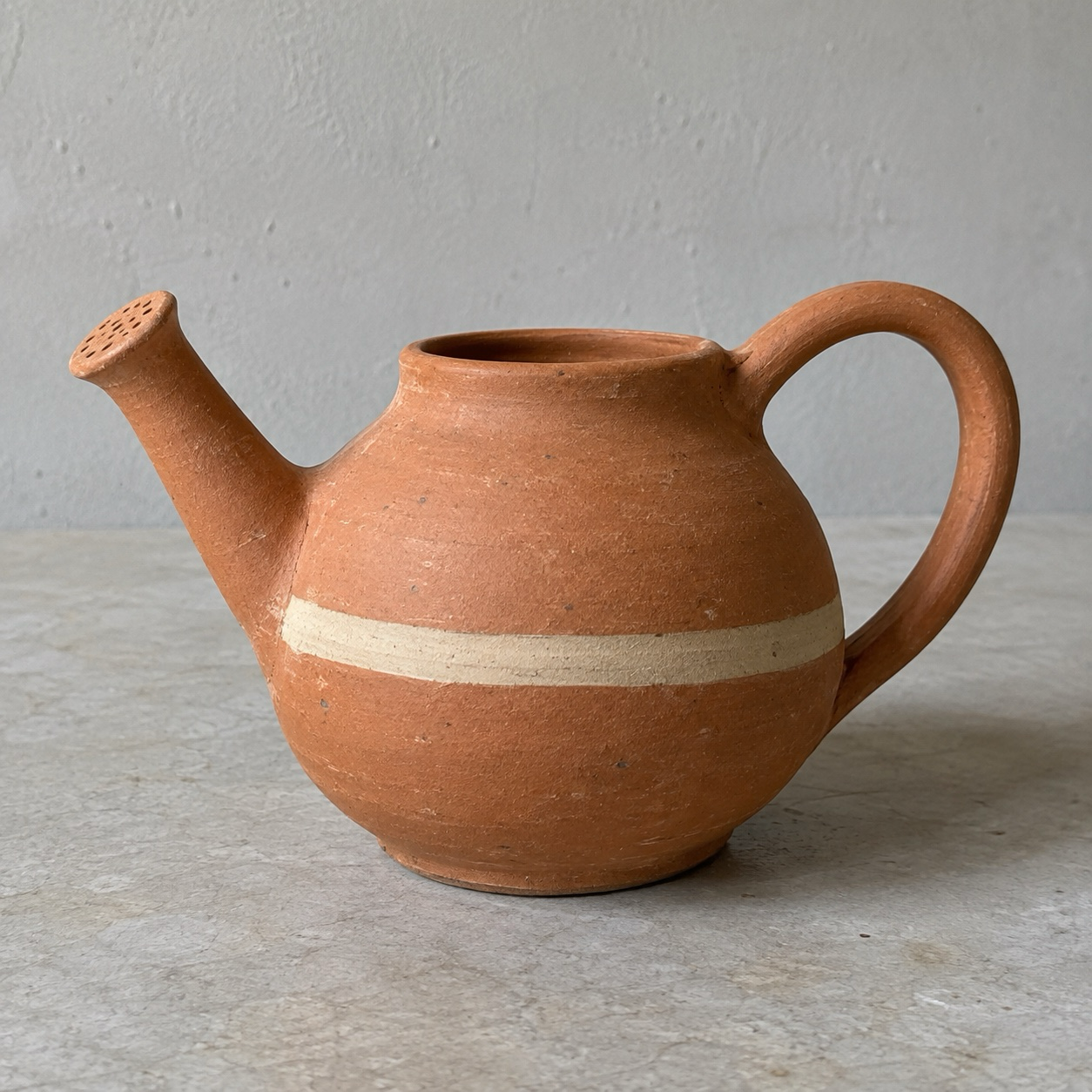 Terracotta watering can on a counter in ordinary daylight; the starting photo before a Clay restyle